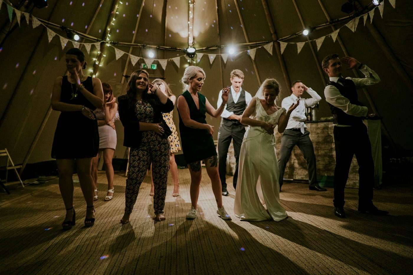 The bride and guests dance inside a tipi tent hung with fabric bunting and fairy lights