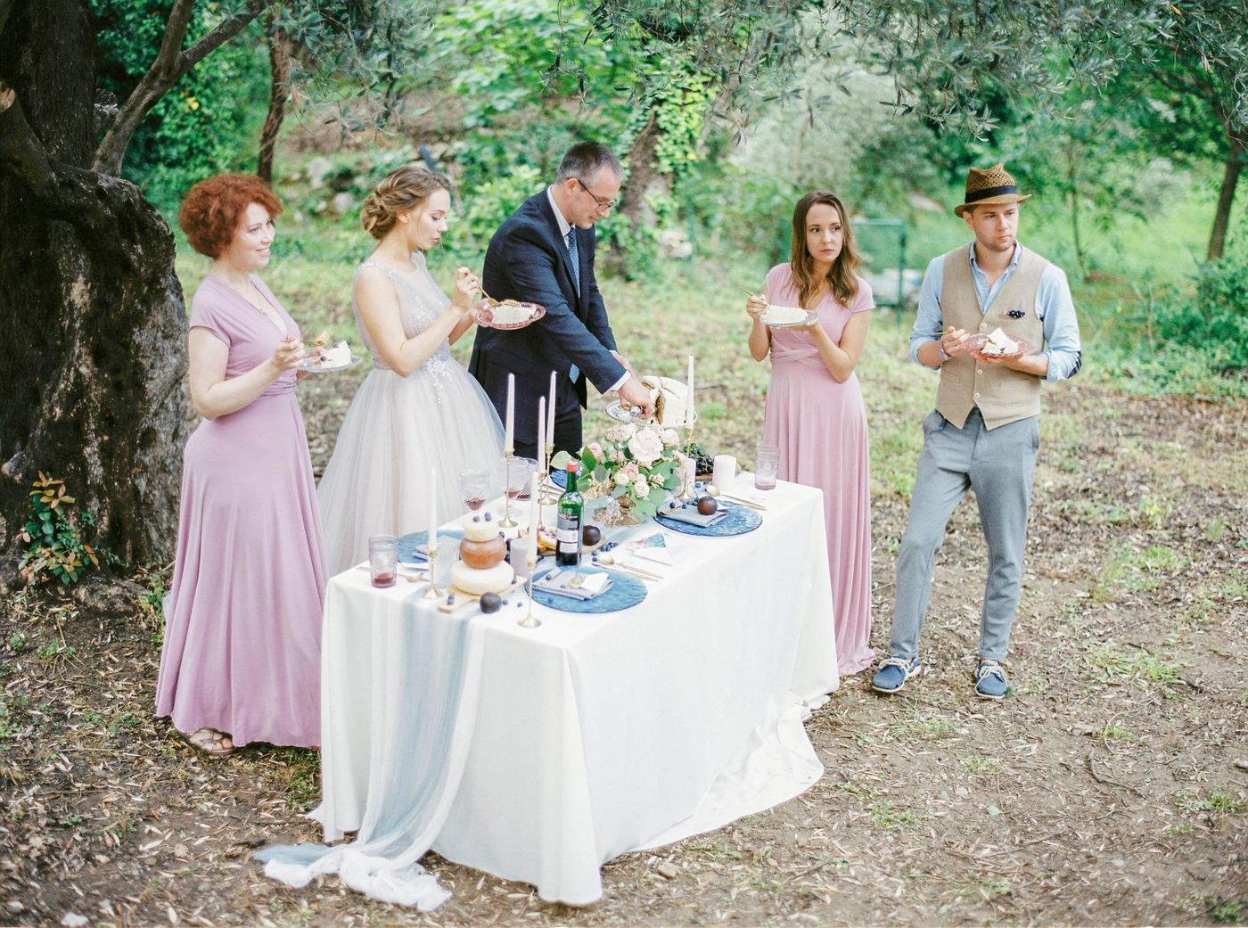 Les mariés et leurs amis mangent du gâteau dans de petites assiettes autour d'une table en plein air sous les oliviers