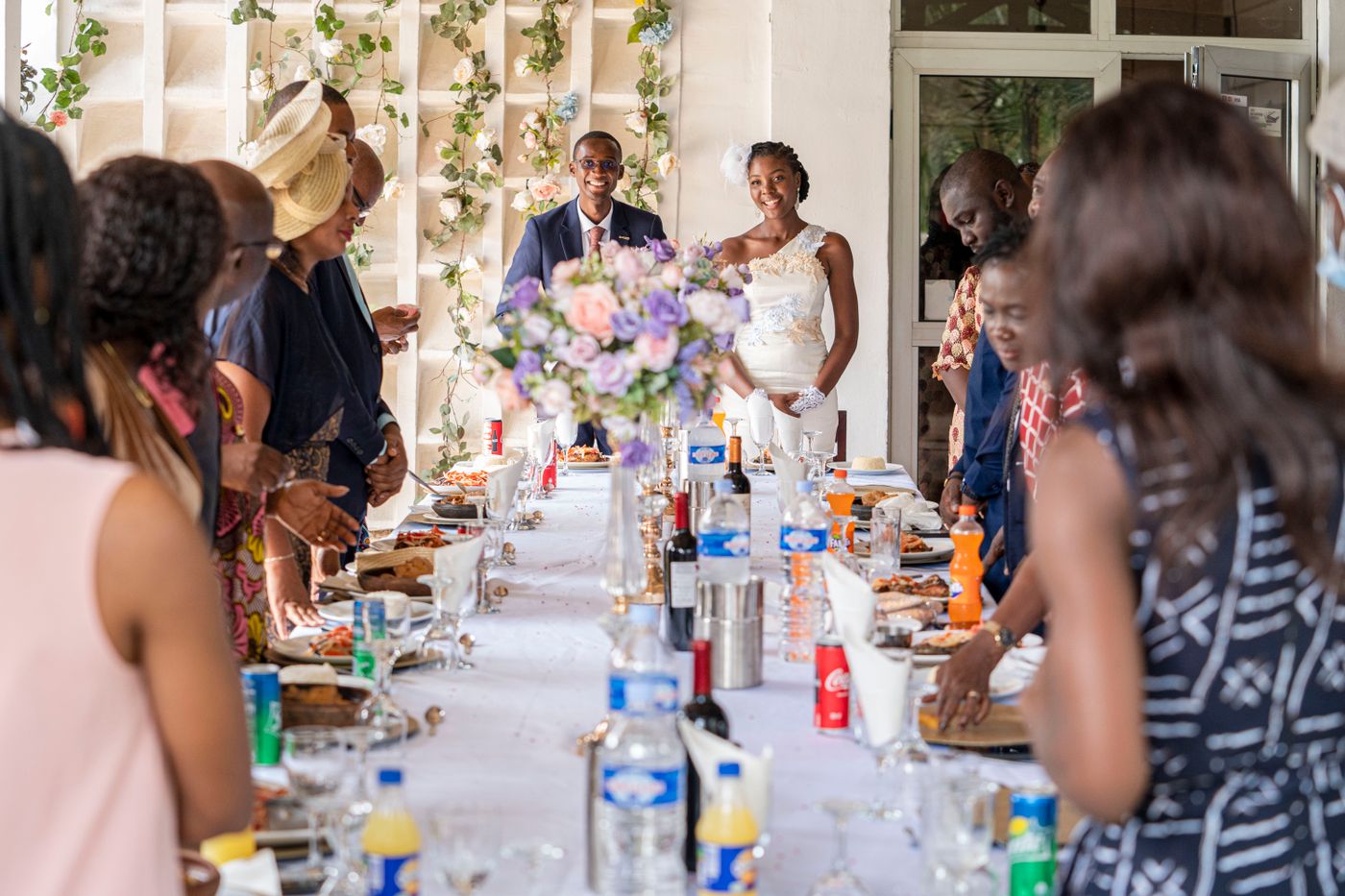 Les mariés sourient au bout d'une longue table pendant que les invités se servent dans des plats à partager