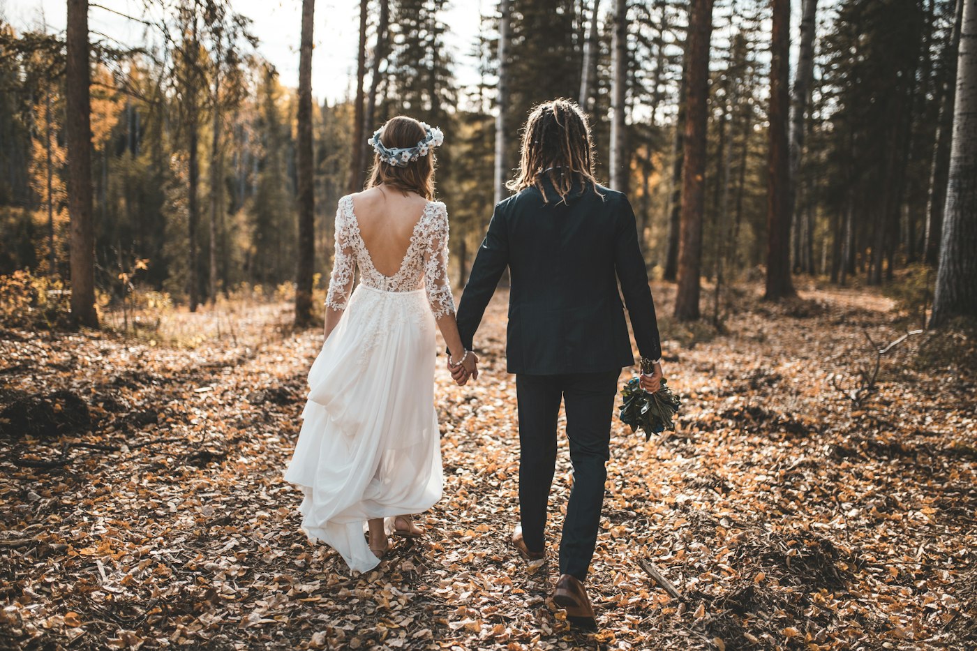Bride and groom walk hand in hand through an autumn forest with fallen leaves