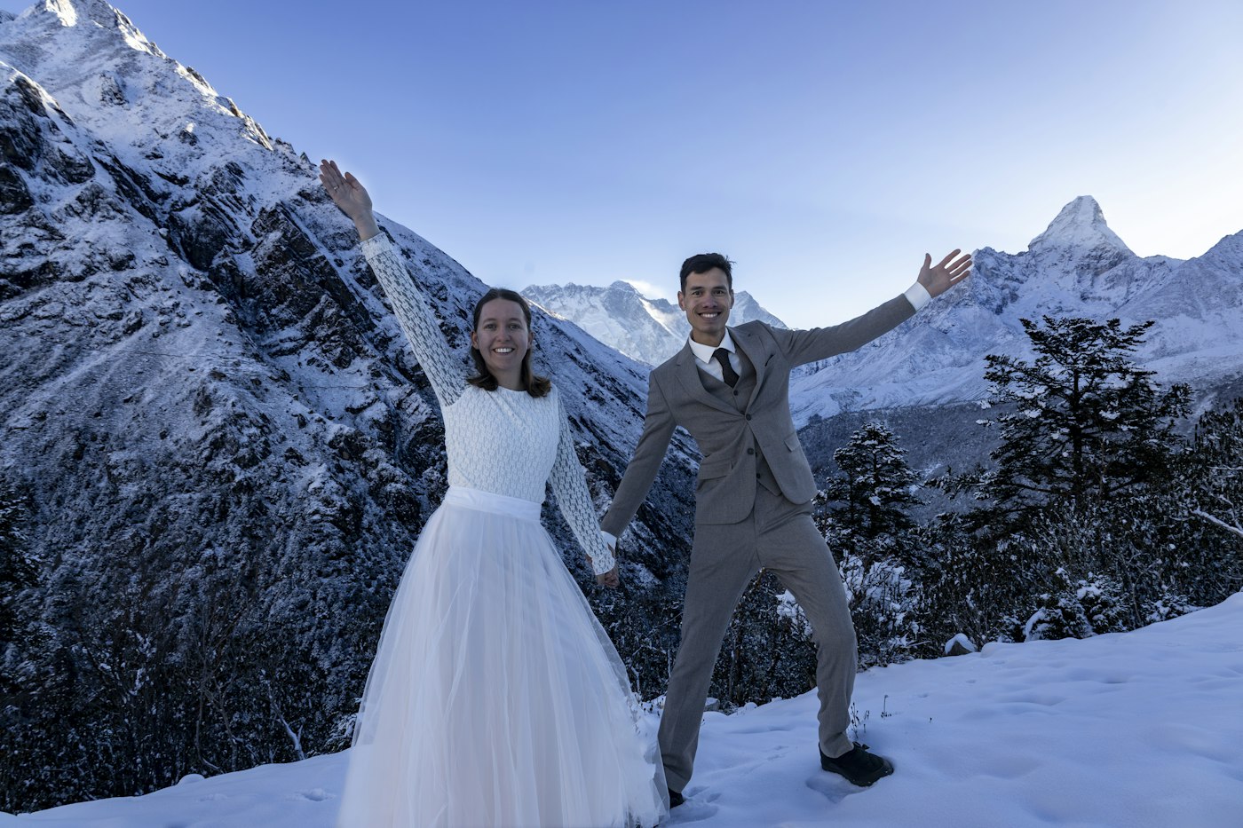 Bride and groom throw their arms wide on a snowy mountainside in winter sun