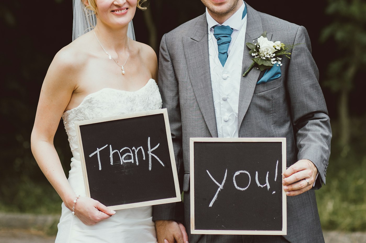 The bride and groom stand side by side holding two small chalkboards that read Thank you