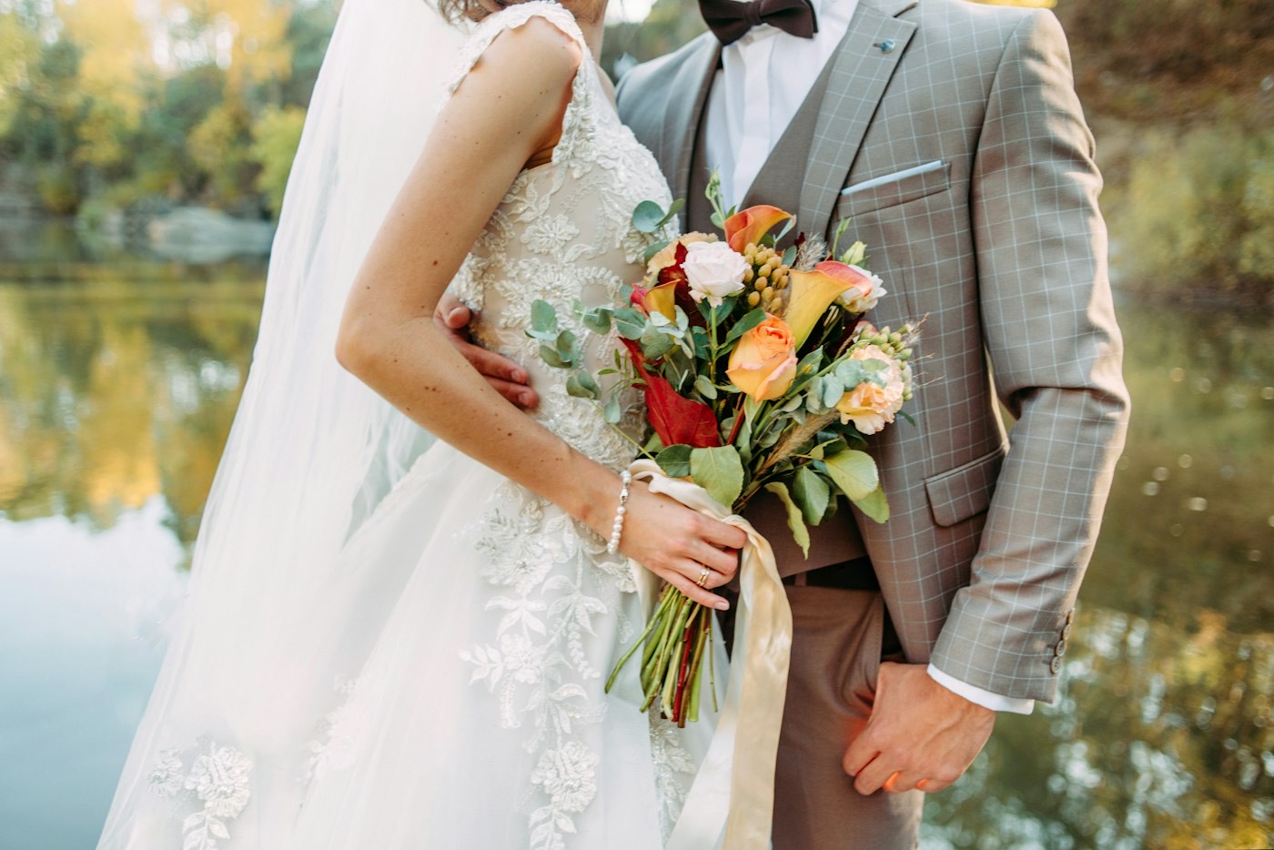 Primer plano de un ramo de novia otoñal con calas naranjas, rosas y eucalipto junto al traje de tweed del novio