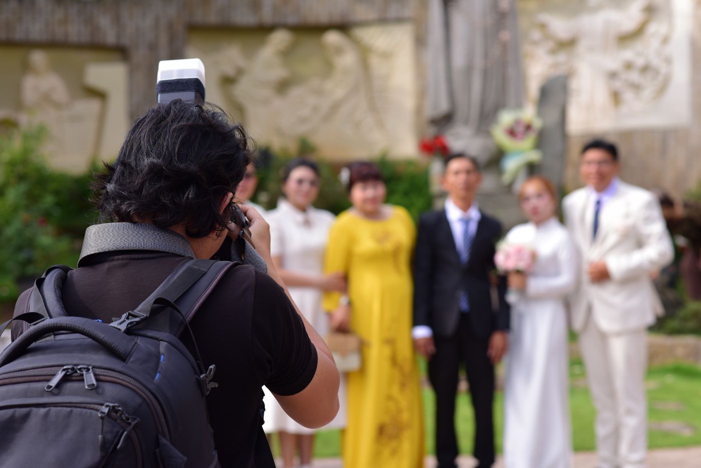 Ein Fotograf mit Rucksack und Blitz fotografiert ein Brautpaar mit Familie im Freien