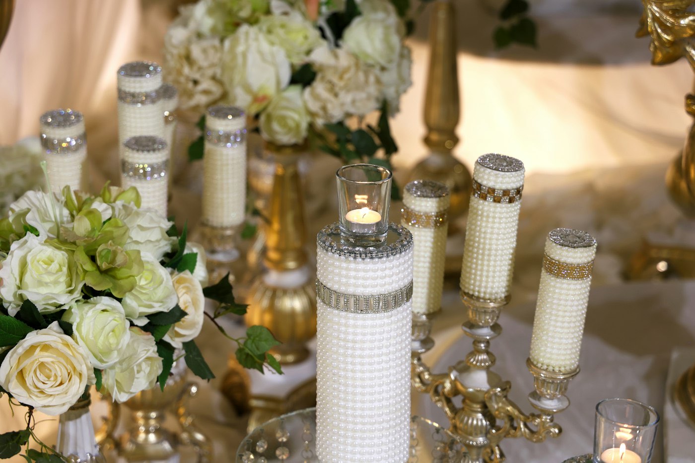 White pillar candles in glass holders between white roses on a reception table