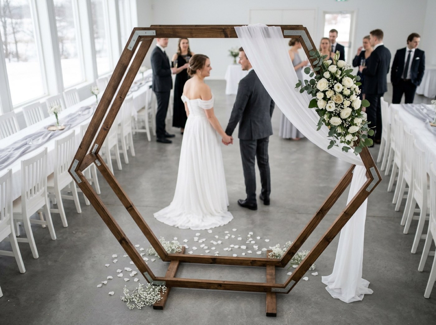 A large stained wooden hexagon arch standing on a lawn, with a sheer white drape and eucalyptus garland on one upper corner