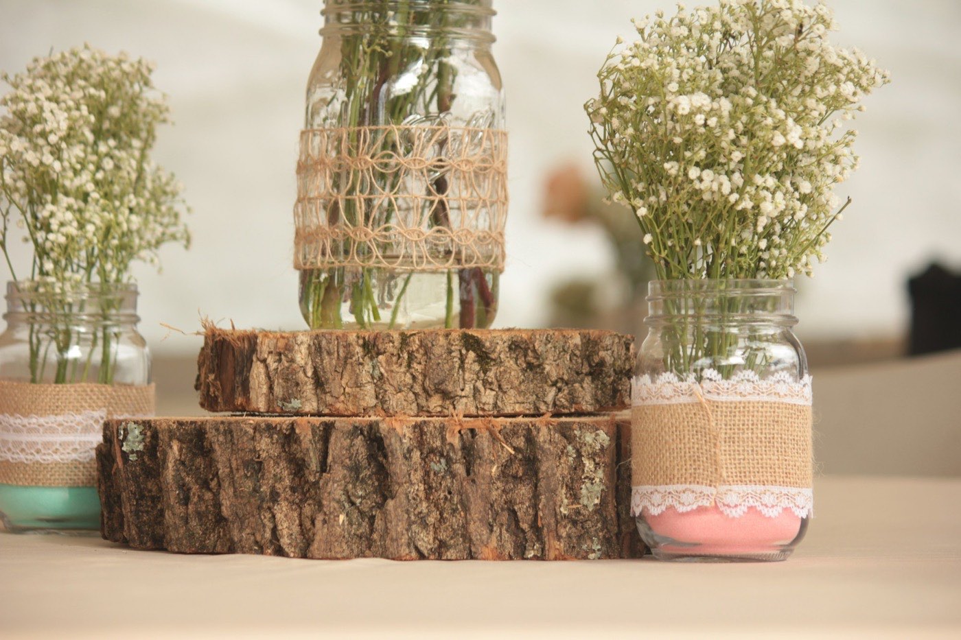 Mason jars wrapped in burlap and lace, filled with baby's breath, on wooden log slices at a rustic wedding reception