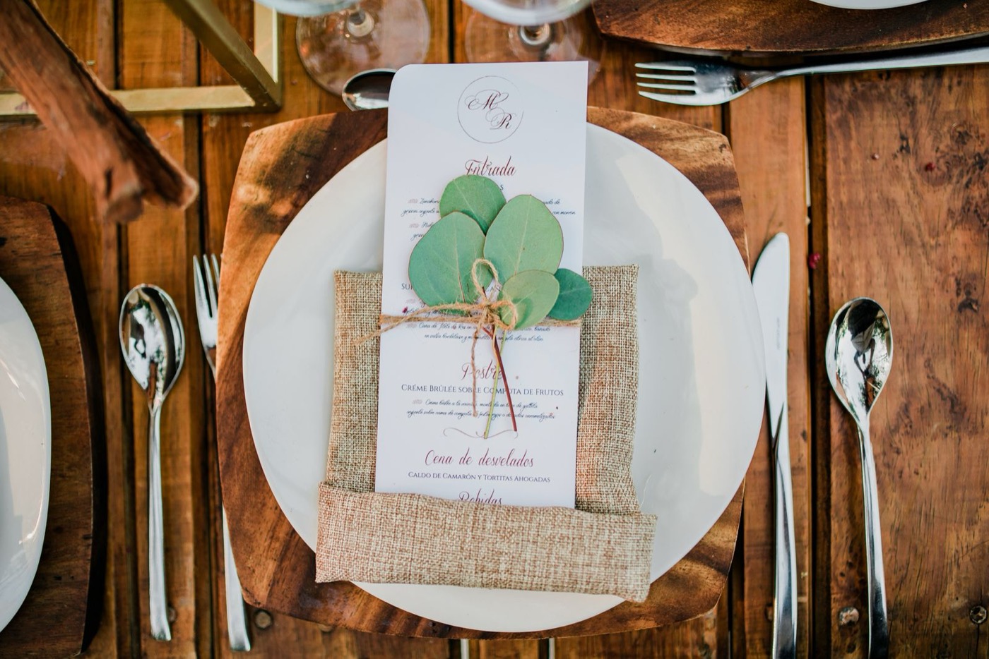 A wedding place setting with a burlap napkin, a printed menu and a sprig of round eucalyptus leaves tied on with a jute twine bow